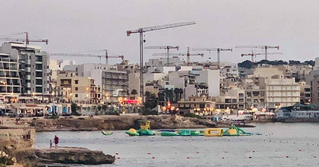 A wide waterfront panorama with cranes and low-rise sprawl