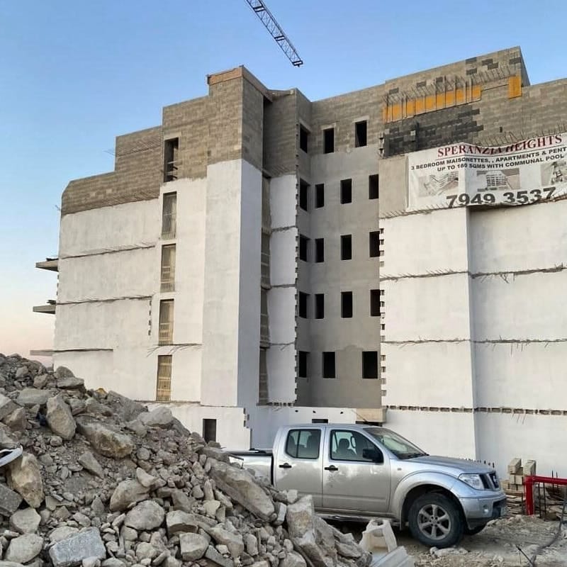 A large concrete building under construction, a pickup parked below