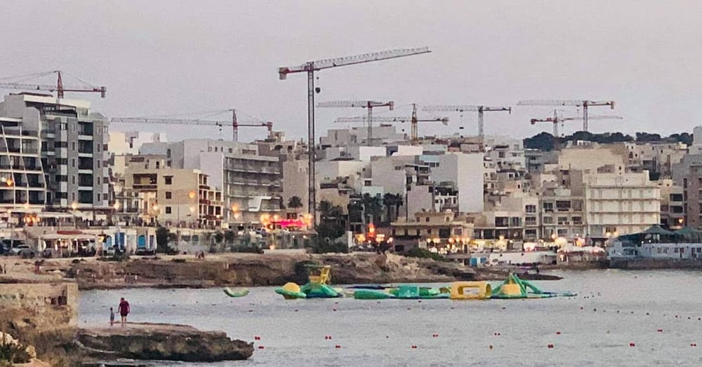 A wide waterfront panorama with cranes and low-rise sprawl