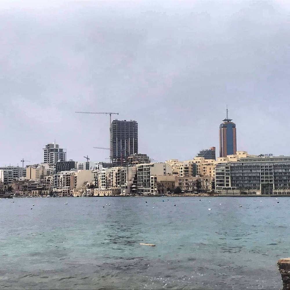 A seafront skyline of towers and cranes